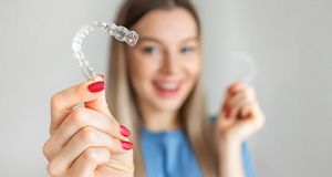 Woman with red nails in blue shirt holding Invisalign to foreground