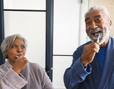 Couple smiling while brushing teeth in bathroom