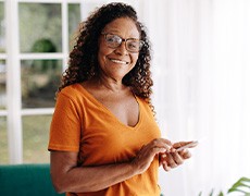 Senior woman with glasses smiling while looking at phone