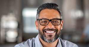 A middle-aged man wearing glasses and smiling after seeing his BlueCross BlueShield dentist in Framingham