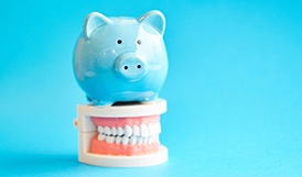 piggy bank atop model teeth for cost of dental implants in Framingham