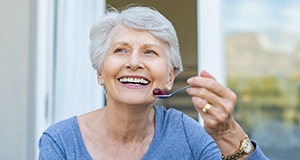 An older woman wearing a blue blouse and eating a spoonful of grapes after receiving dentures in Framingham