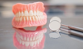 Two dentures sitting on a glass countertop next to a dental mirror