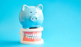 piggy bank atop dentures representing cost of dentures in Framingham 
