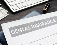 Dental insurance forms on table with cash, keyboard, and pens