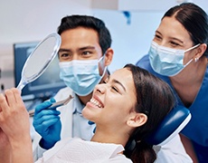 Patient smiling at reflection in mirror with dentist and dental assistant