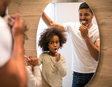 Father and daughter brushing their teeth together in bathroom
