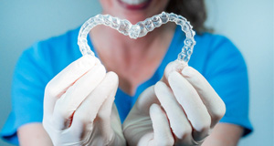 Woman wearing white gloves smiling holding Invisalign in heart shape