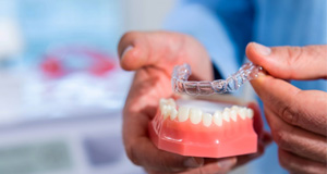 Hands placing Invisalign over lower arch of model teeth