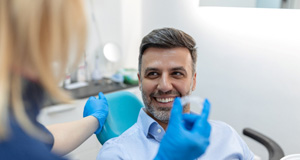 Man in dental chair smiling and dentist holding Invisalign