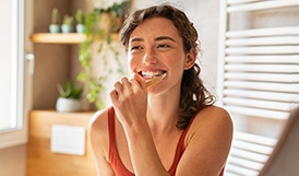 Woman smiling while brushing her teeth in bathroom