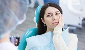 Woman with toothache holding cheek while looking at dentist