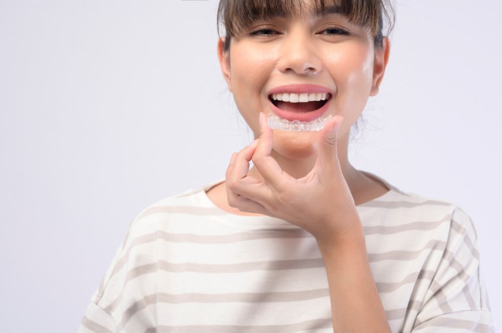 Woman smiling while putting on Invisalign clear aligners
