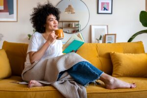 Woman on couch holding mug of coffee while reading 
